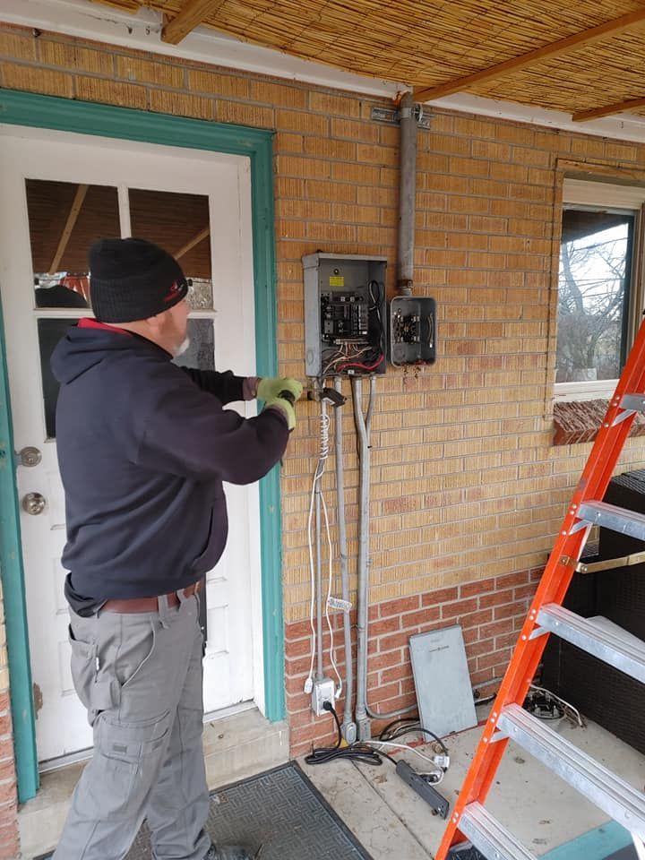 A man is working on a electrical box on the side of a brick building.