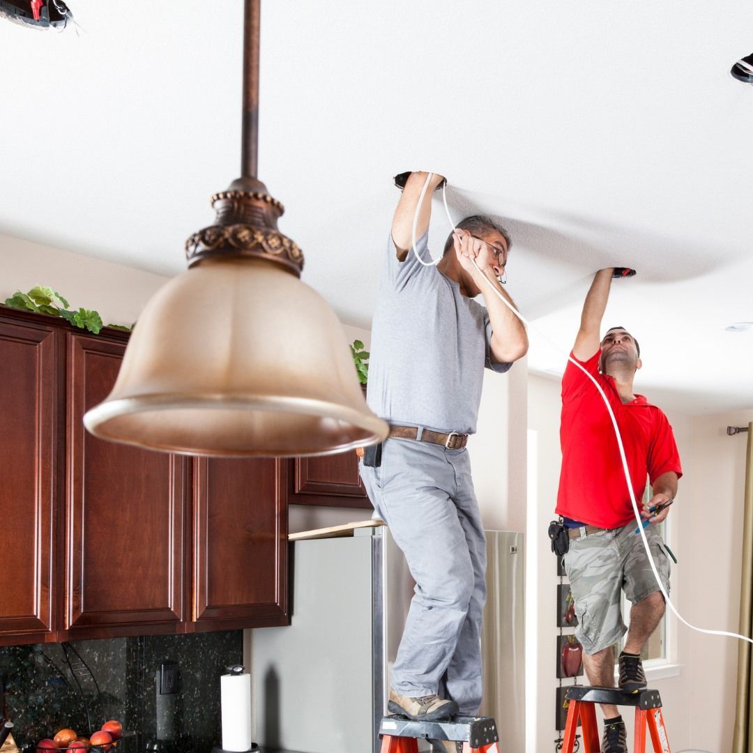 Two men are working on a ceiling in a kitchen