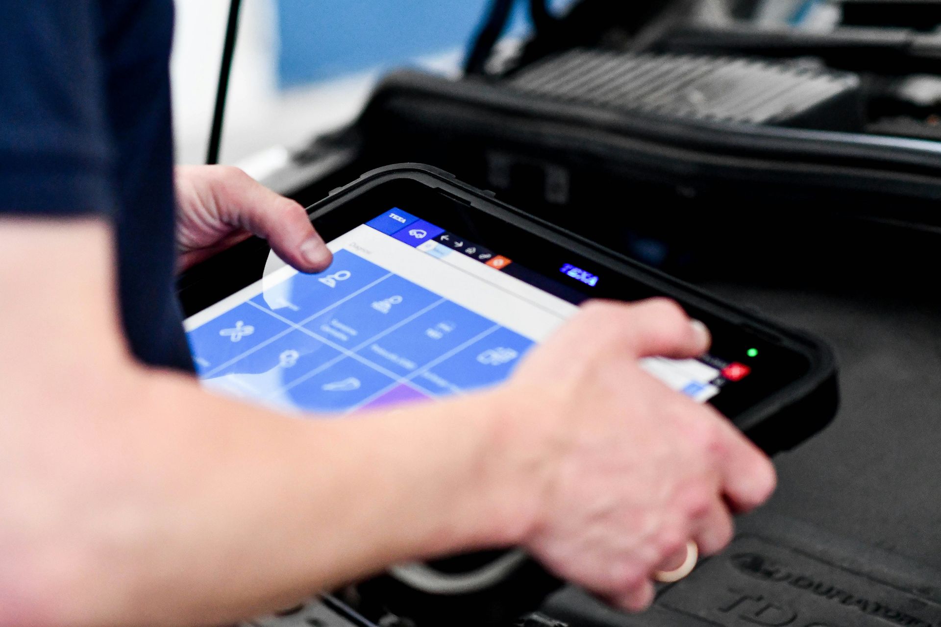 Hands using a touchscreen device in a car, with a blue app interface visible.