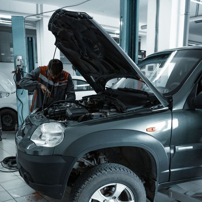 Mechanic working on a gray SUV with the hood open in an auto repair shop