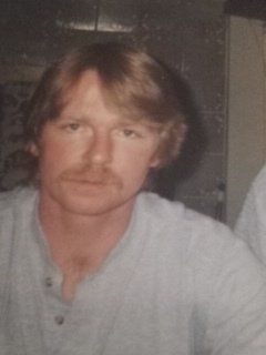 A man with a beard is wearing a white shirt and looking at the camera.