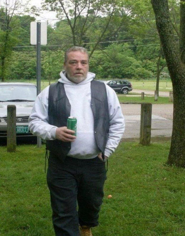 A man in a white sweatshirt and a black vest is holding a can of soda.