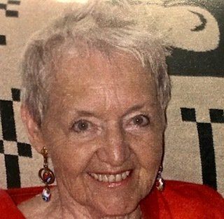 An elderly woman wearing a red shirt and earrings is smiling for the camera.