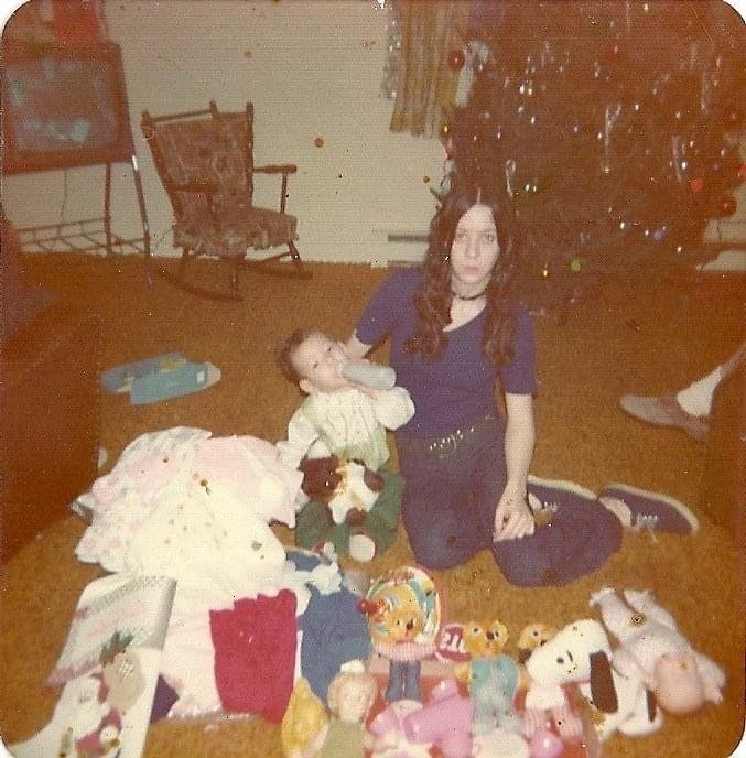 A woman sits on the floor holding a baby in front of a christmas tree