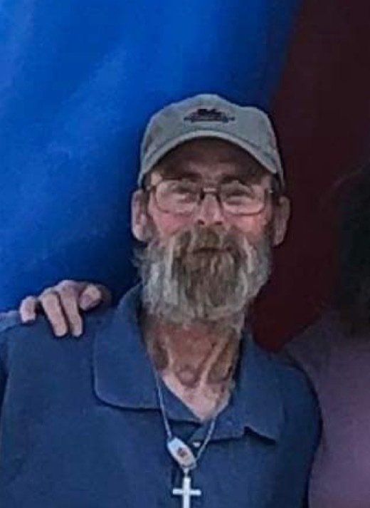 A man with a beard and glasses is wearing a hat and a cross necklace.