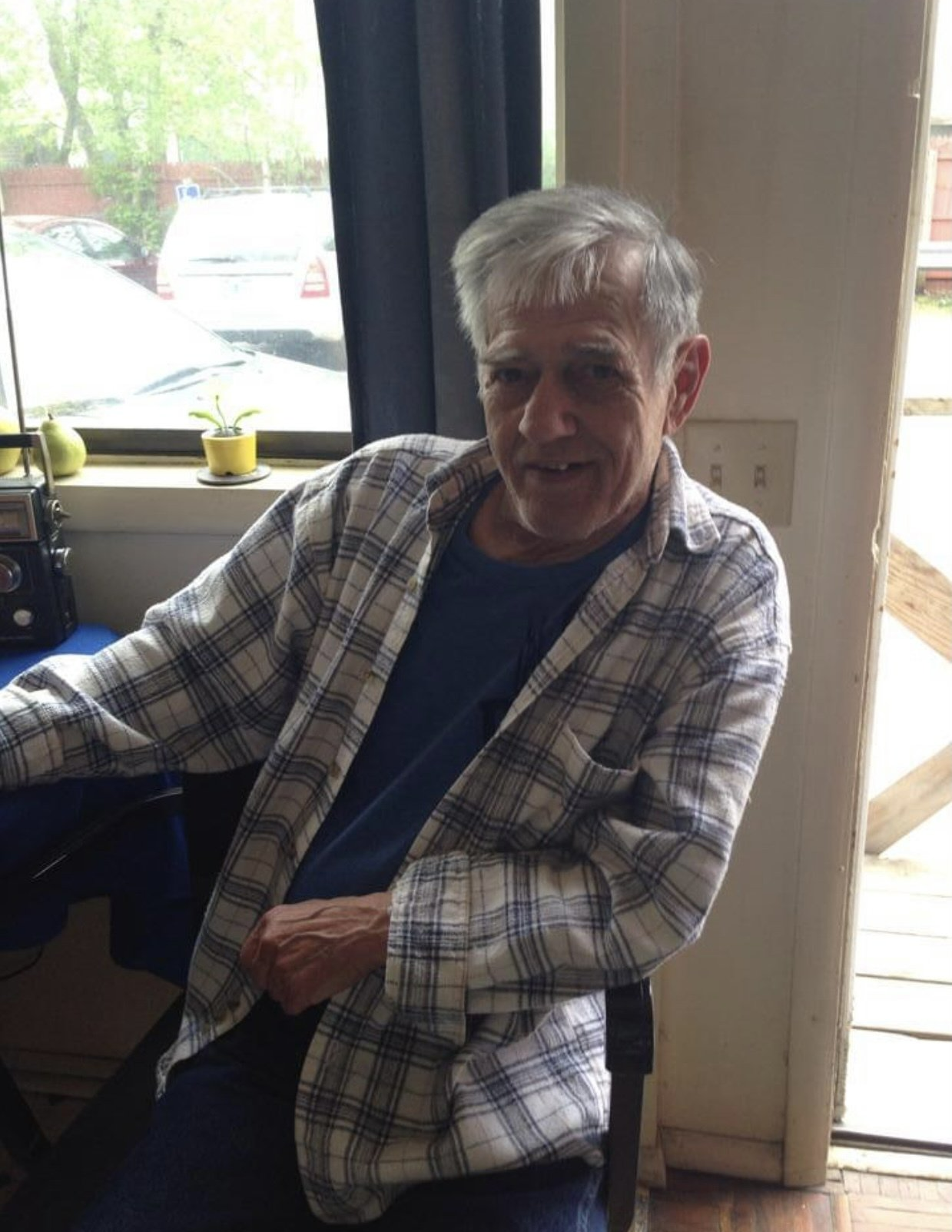 A man in a plaid shirt is sitting in front of a window