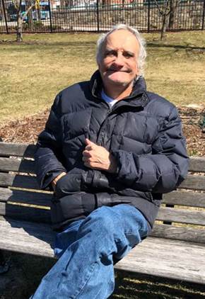 A man in a black jacket is sitting on a park bench.