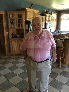 A man in a pink shirt and khaki pants is standing in a kitchen.
