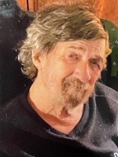 A man with a beard is sitting in a chair and looking at the camera.