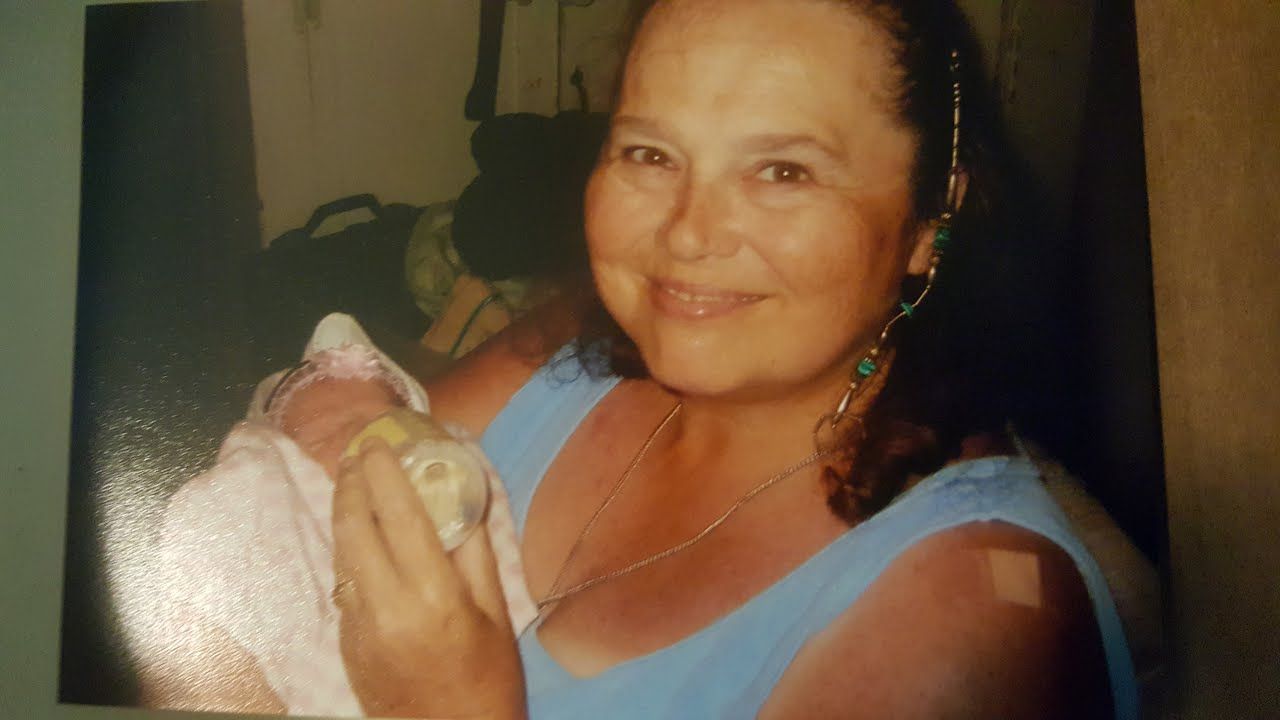 A woman in a blue shirt is holding a baby in her arms.