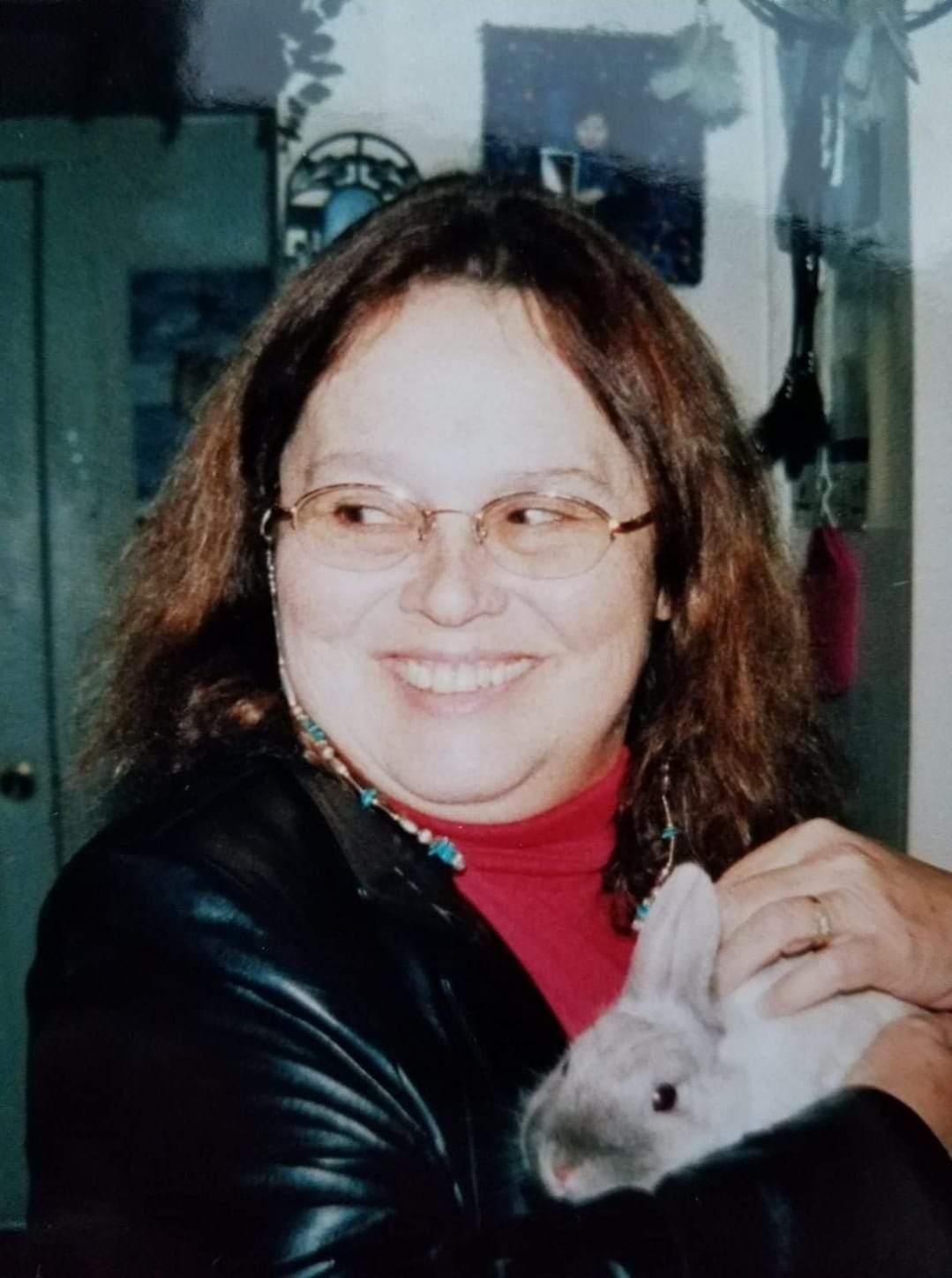 A woman is holding a small rabbit in her arms and smiling.