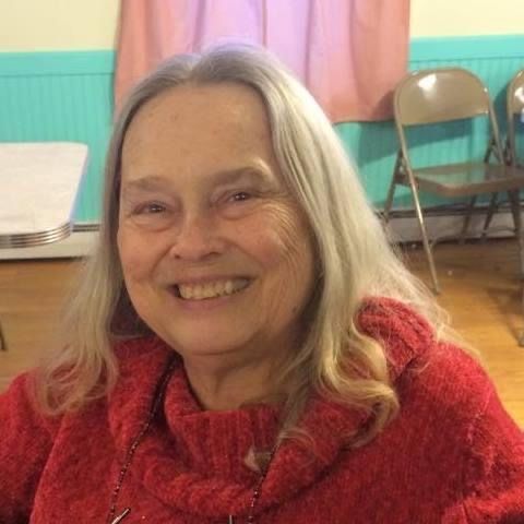 A woman in a red sweater is smiling in a room.