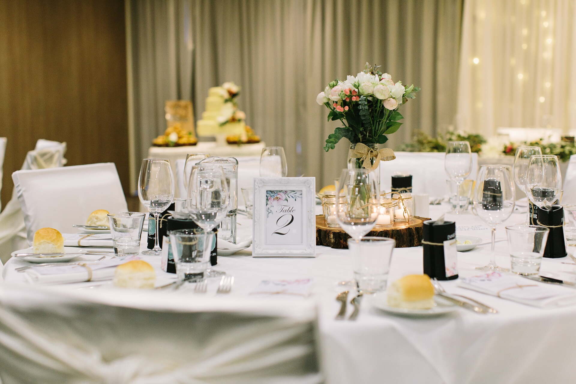 A table set for a wedding reception with a cake in the background