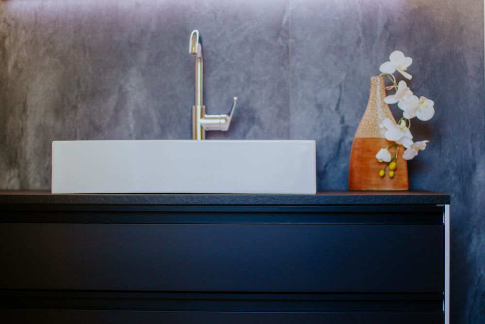Ein Waschbecken im Badezimmer mit Wasserhahn und einer Vase mit Blumen auf der Ablage.