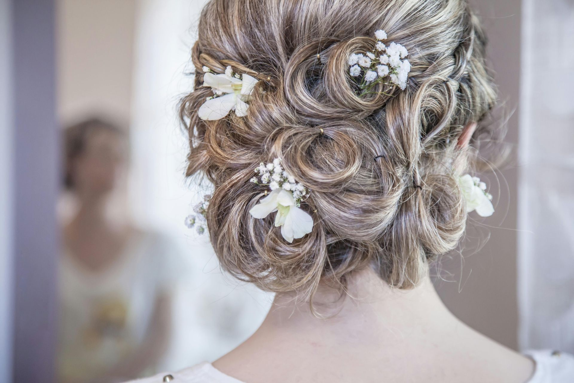 Woman's updo hairstyle with white flowers and a blurred reflection in a mirror.