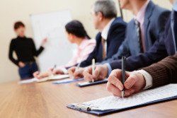 a group of people are sitting at a table writing on a clipboard .