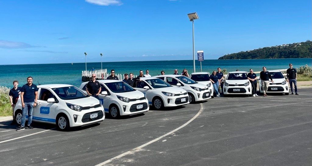 a group of people standing next to a row of white cars in a parking lot .