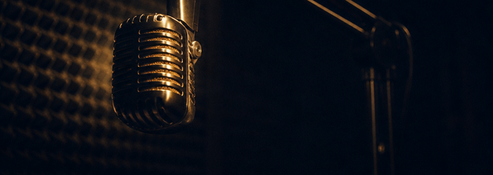 A vintage ribbon microphone on a boom arm in a darkened recording booth