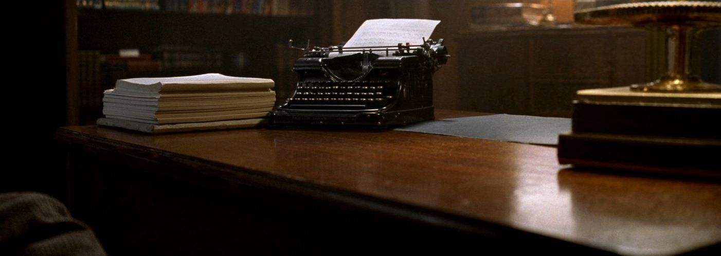 An antique manual typewriter and a stack of typed pages on a desk under a warm lamp