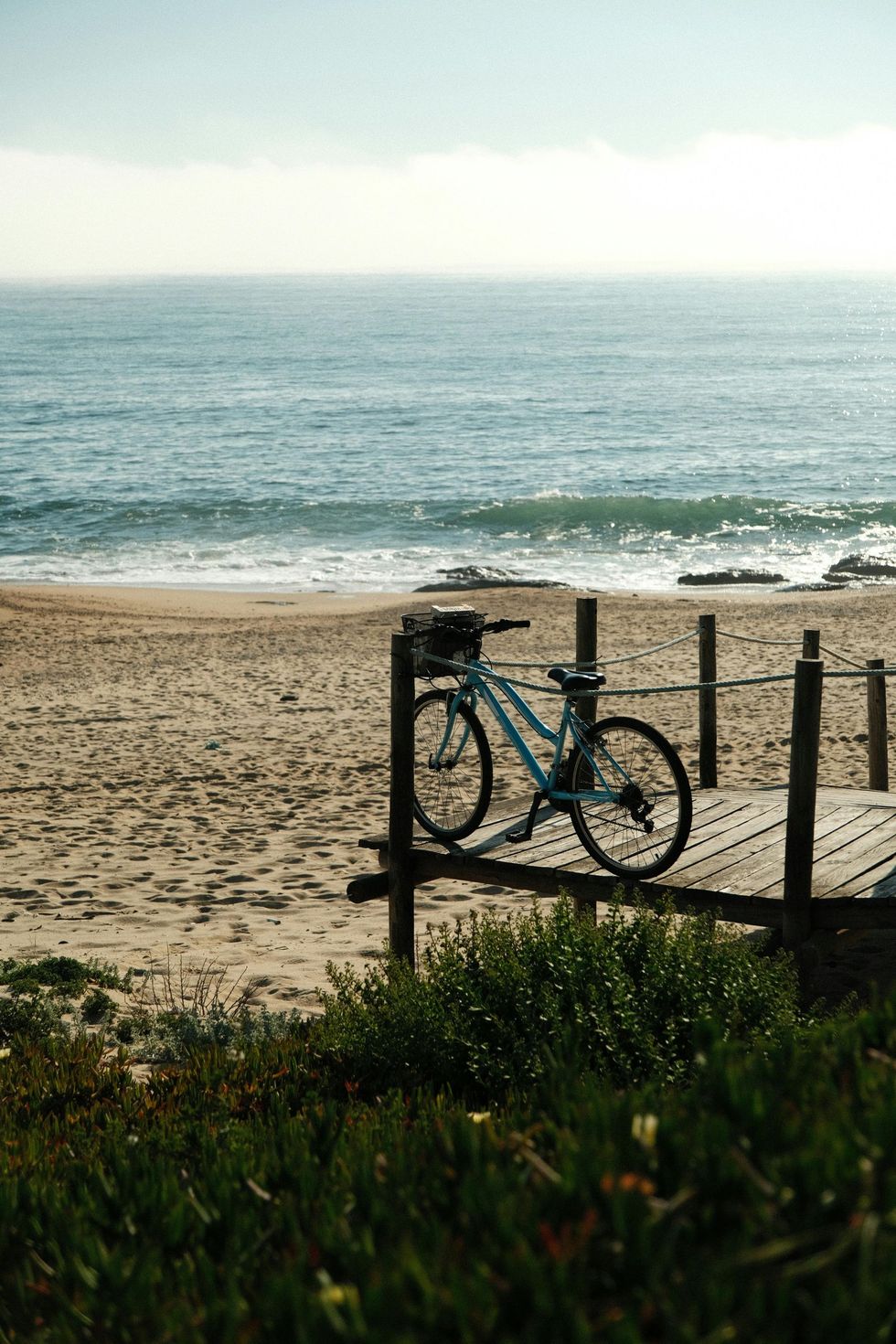 Blue bicycle on a wooden deck overlooking a sandy beach and calm ocean.