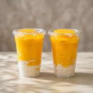 Two clear cups of mango dessert with yellow puree and white tapioca pearls on a table