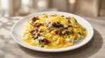 Cheesy scrambled eggs topped with herbs and sausage on a white plate
