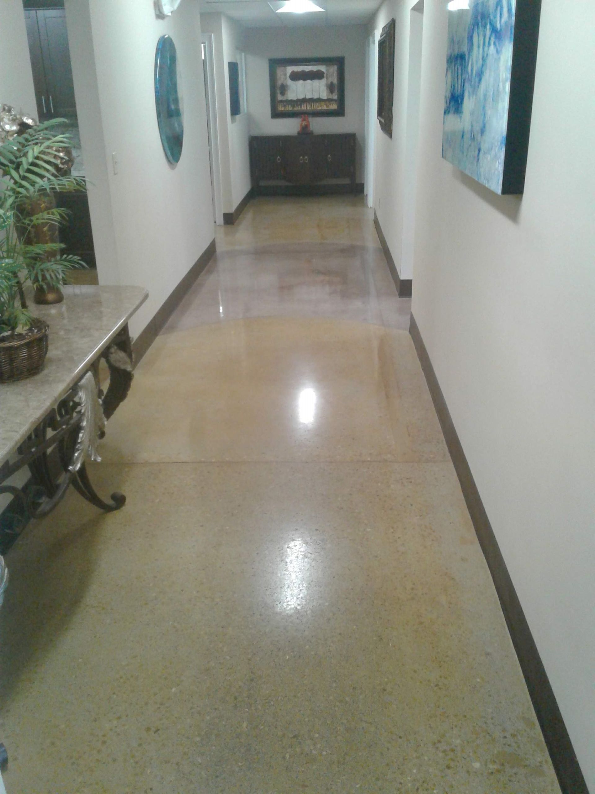 Narrow hallway with polished floor, wall art, and a bench at the left end