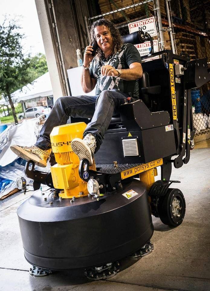 Person riding a large floor-polishing machine in an industrial setting, talking on a phone.
