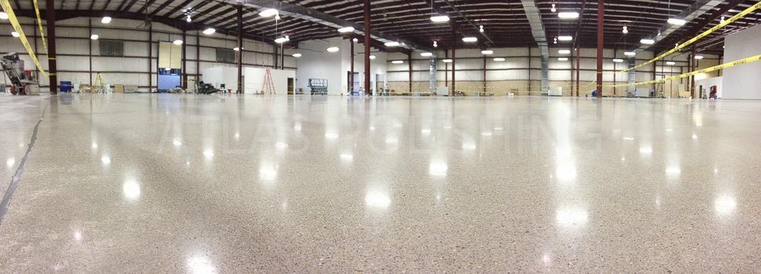 Spacious empty warehouse with polished concrete floor and overhead lights, reflecting the interior.