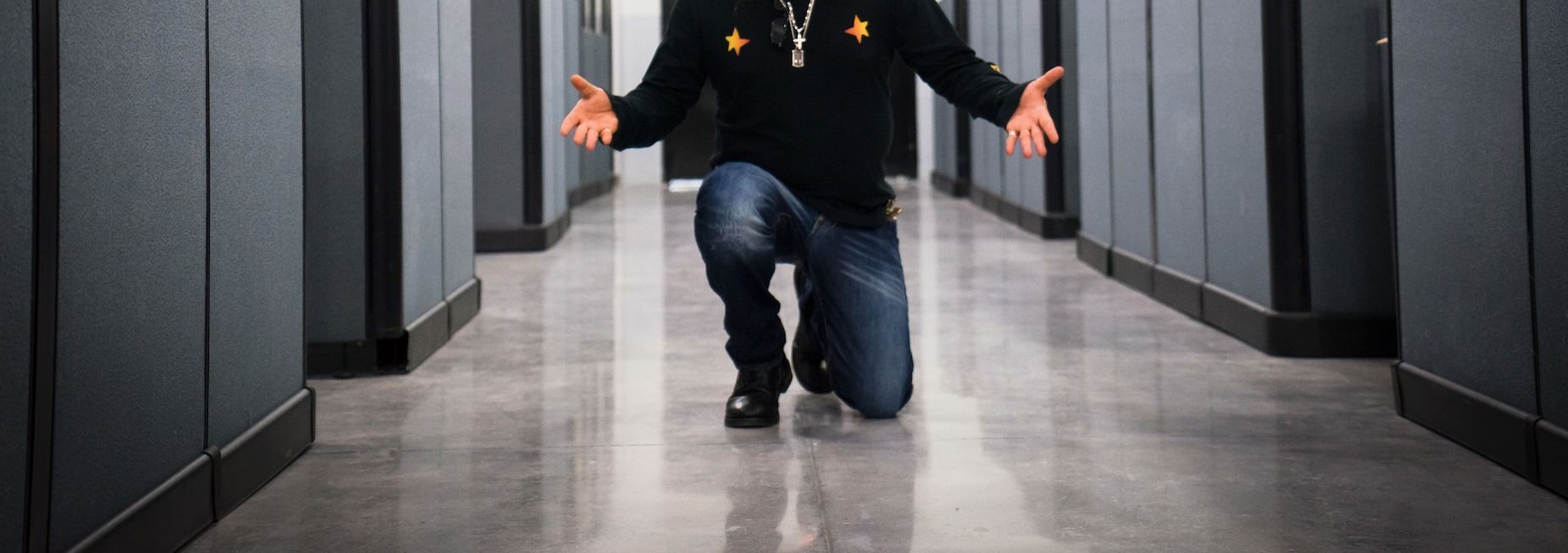 Person kneeling in a hallway between gray office cubicles with arms outstretched