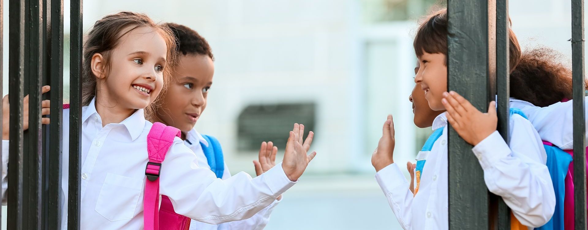 a group of children are waving at each other through a fence .