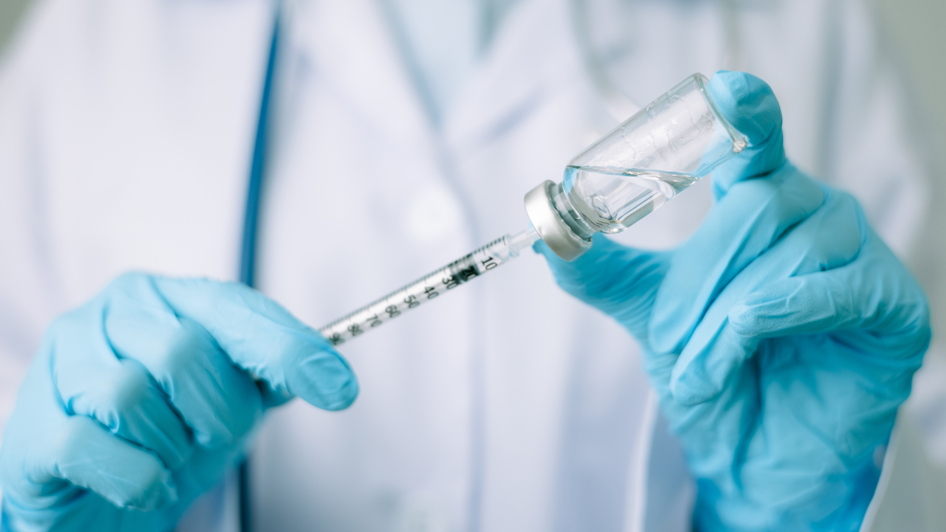 Gloved hands preparing a syringe and vial with vaccine solution in a clinical setting