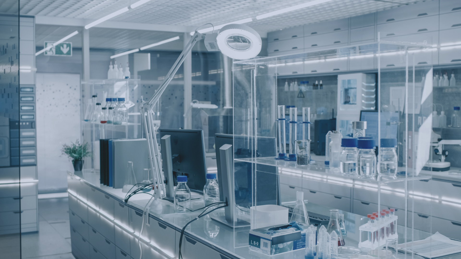 Modern laboratory with glass walls, microscopes, monitors, and lab equipment on stainless steel counters.