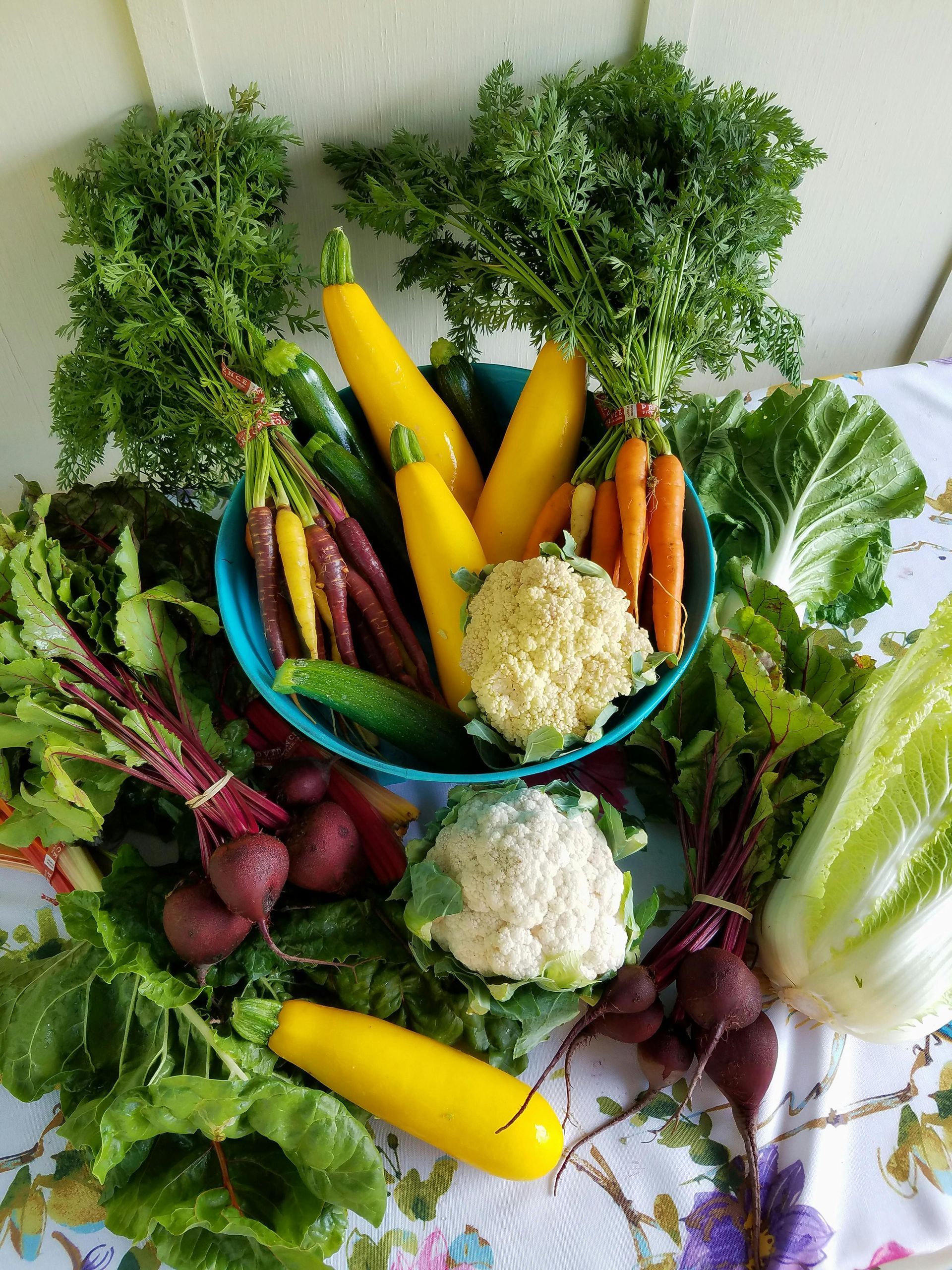 Un bol de légumes est posé sur une table entouré d'autres légumes.