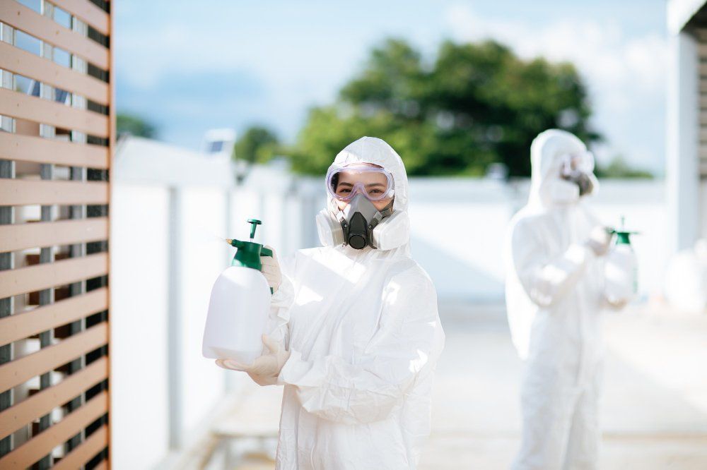 Workers in white protective suits spraying disinfectant outdoors near a building