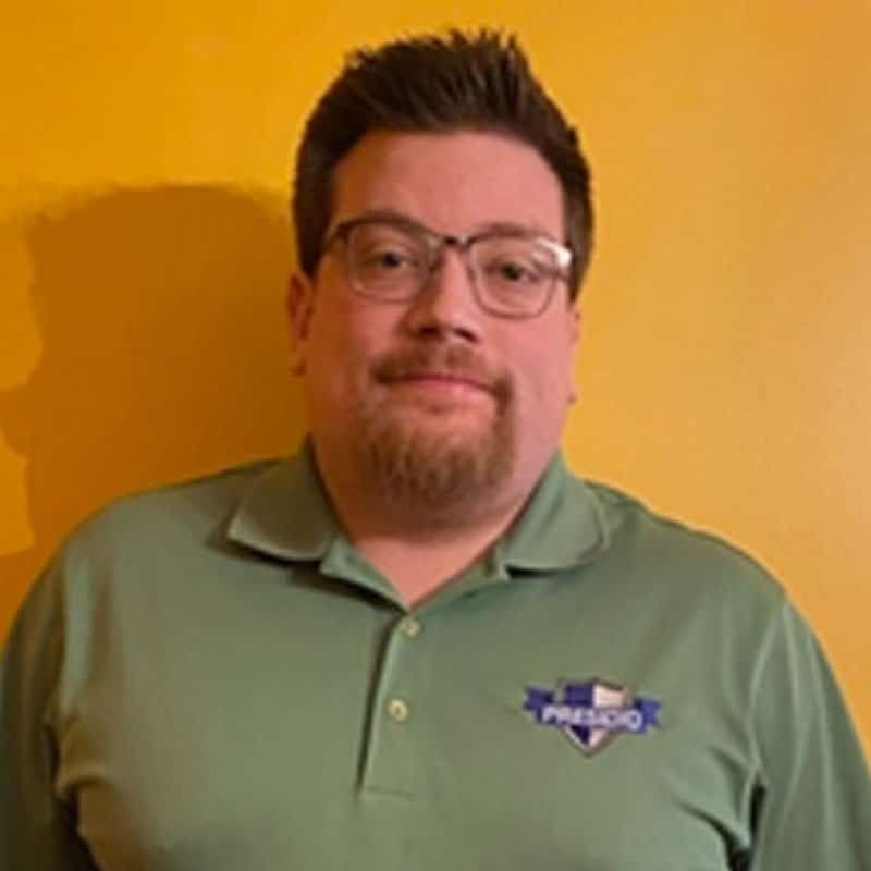 Man wearing glasses and a green polo shirt standing against a yellow wall
