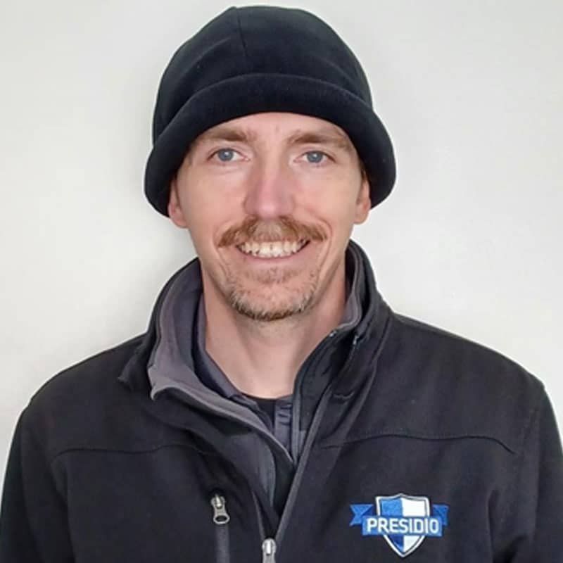Smiling person in a black beanie and jacket with a Presidio logo against a white background