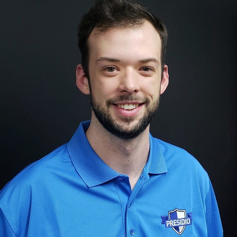 Smiling man in a blue polo shirt with a Presidio logo against a dark background