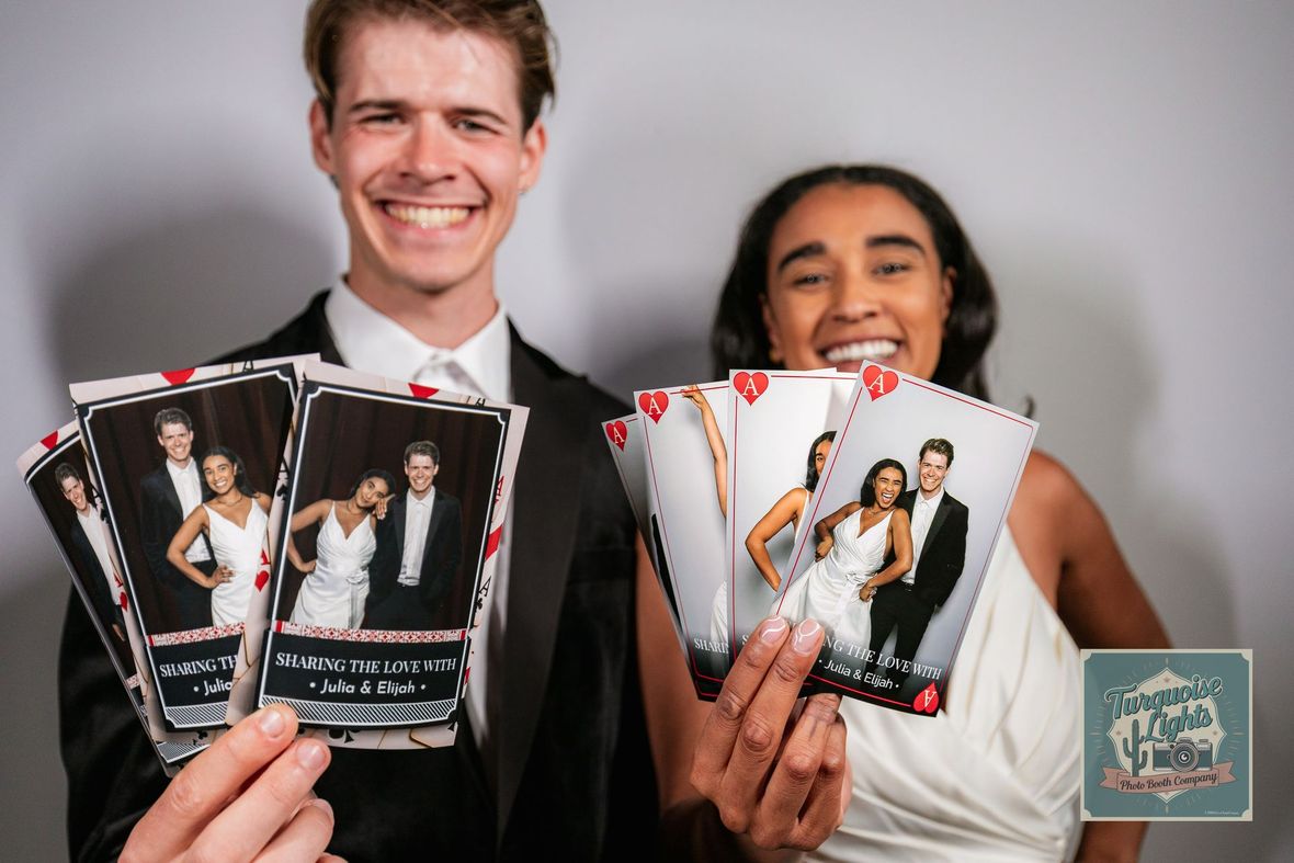 Two smiling people hold up printed photo strips at an event backdrop.