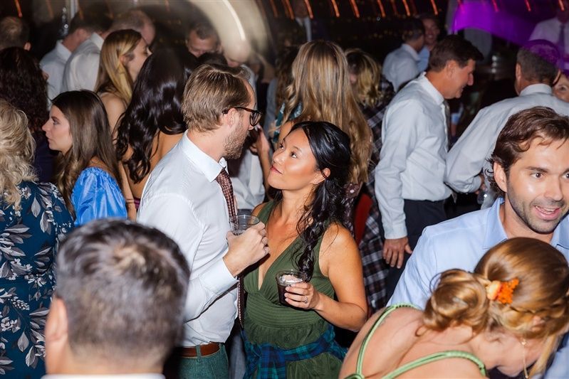 People dancing at a party: woman in green dress talking to a man with glasses; other guests blurred.