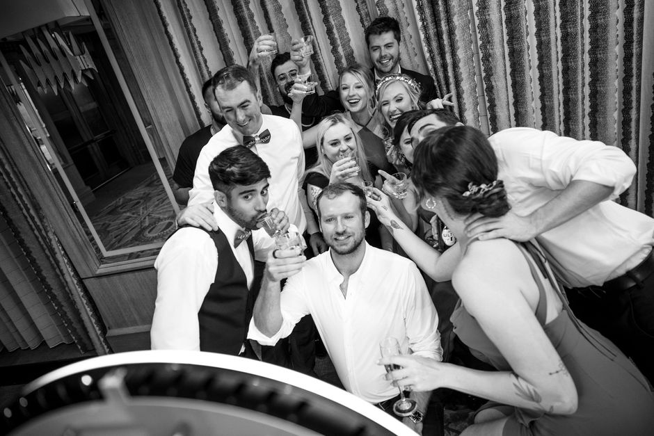 Group posing and laughing around a photobooth  in a black-and-white indoor scene