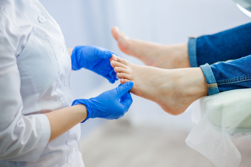 A podiatry doctor, wearing blue gloves, examines a patient's foot.