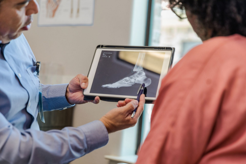 Doctor showing a foot X-ray on a tablet during a consultation. Doctor showing a foot X-ray on a tablet during a consultation.