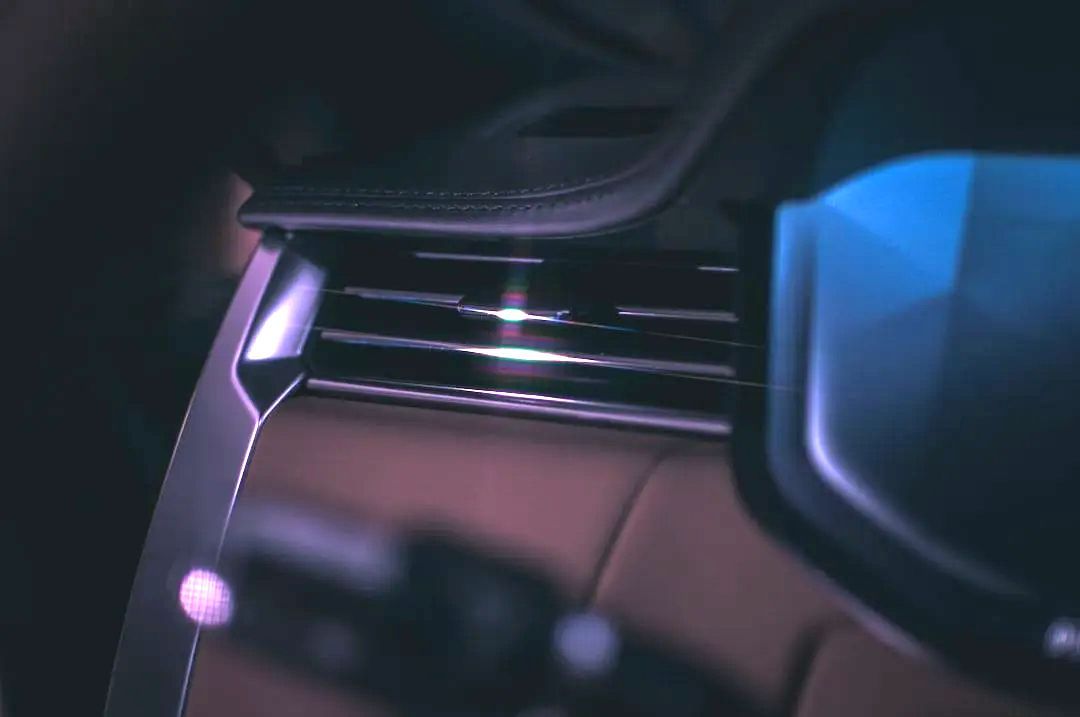 Car interior with metallic air vent, brown leather, and blue screen.