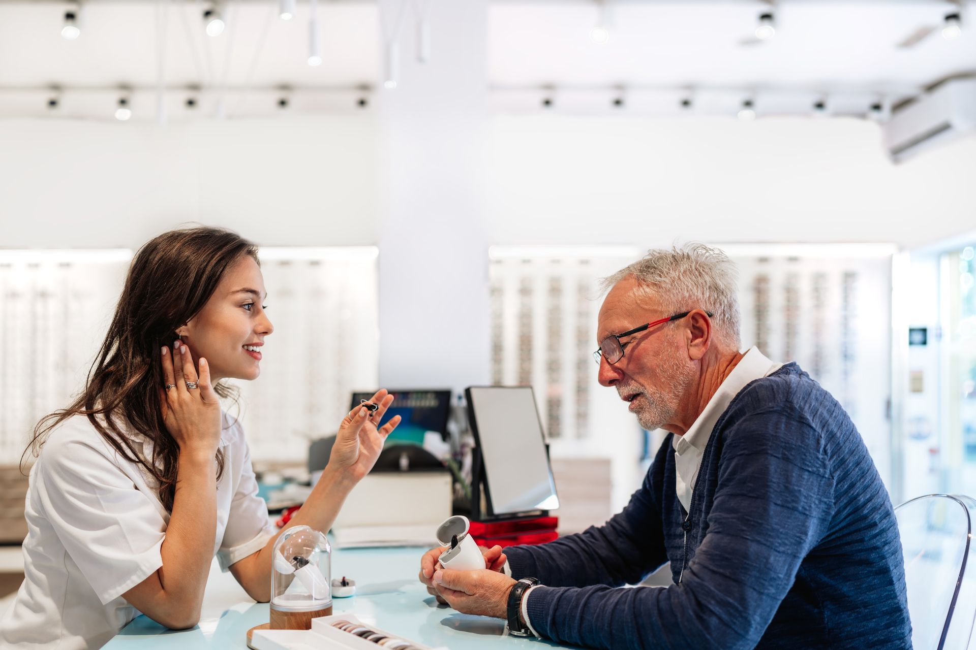 Young audiologist showing hearing aid device to senior man.