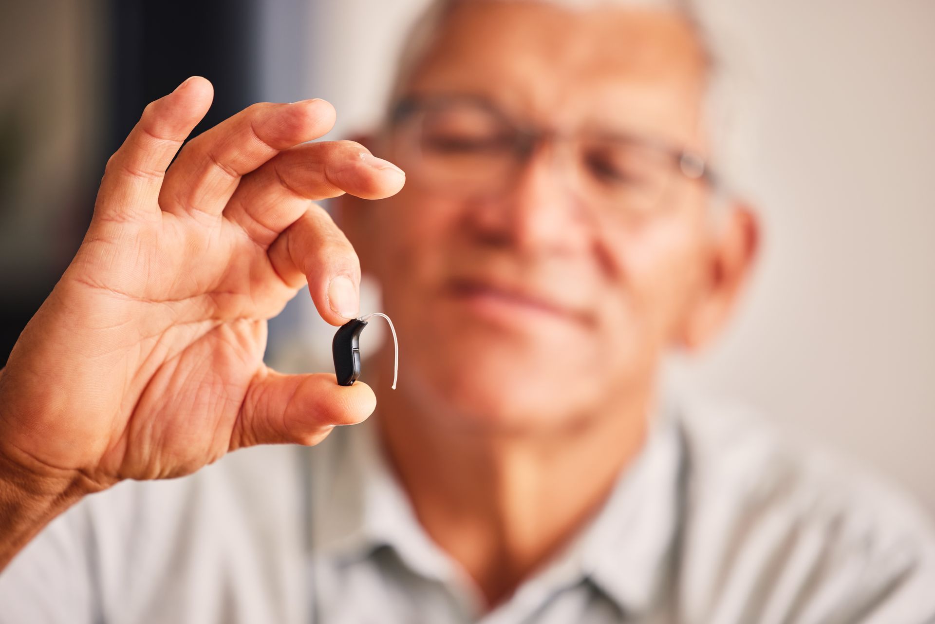 Senior man holding a small behind-the-ear hearing aid between his fingers Senior man holding a small behind-the-ear hearing aid between his fingers