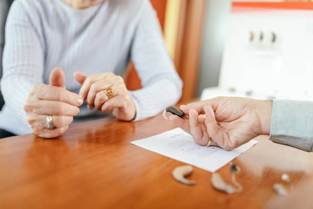 A woman is selecting a hearing aid device at a hearing aid clinic with professional guidance.