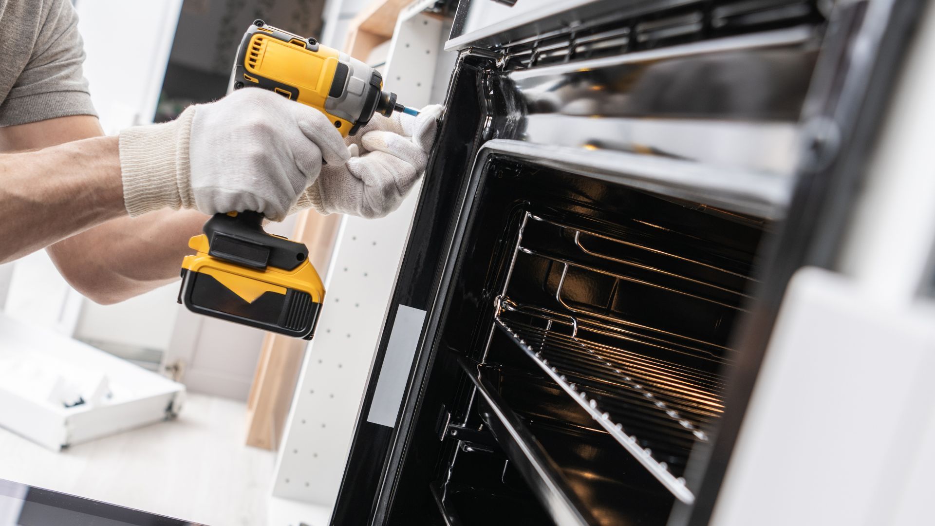 A man is fixing an oven with a drill.