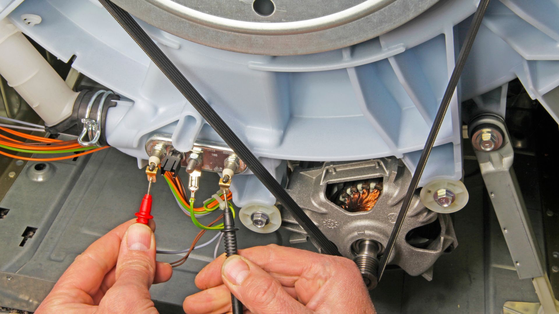 A person is working on a washing machine with a voltmeter.