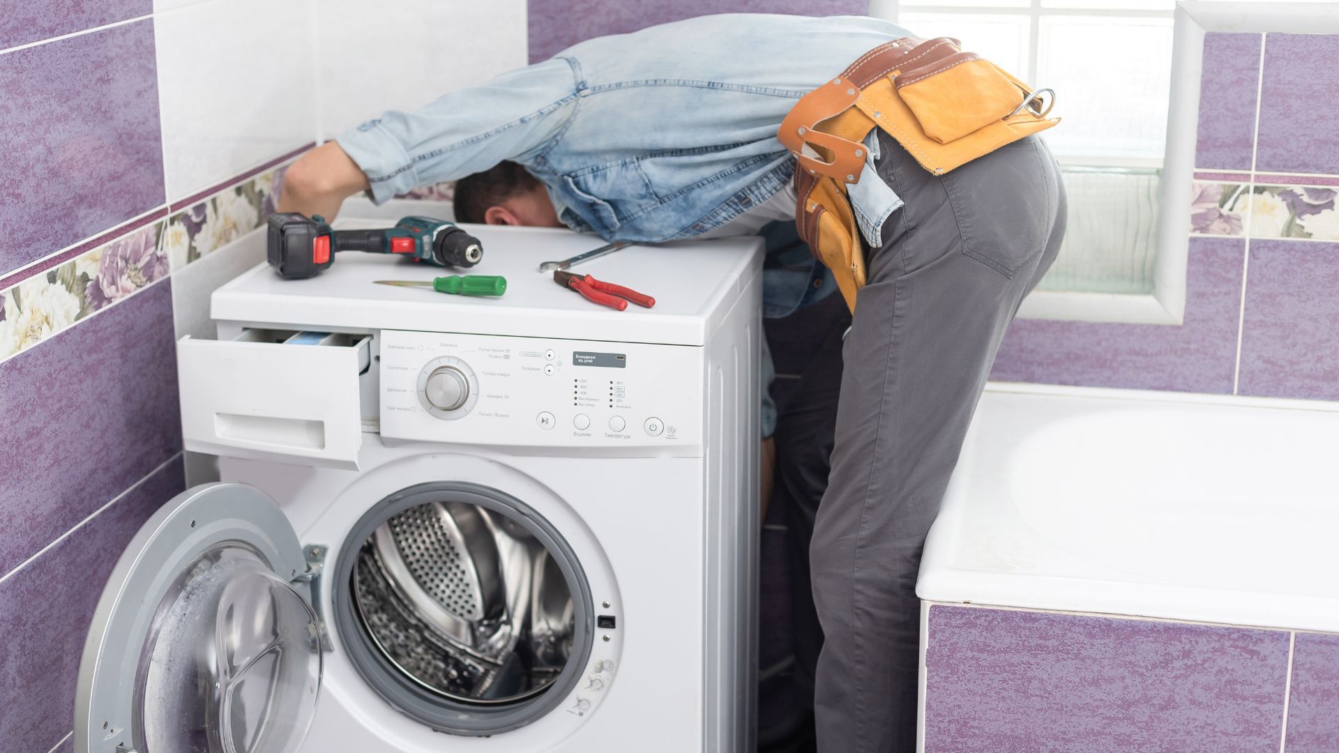 A man is fixing a washing machine in a bathroom.